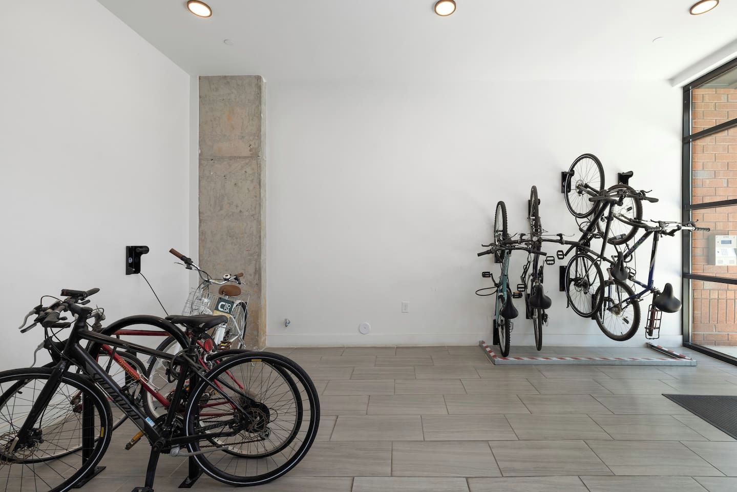 A room with bicycles parked against the wall, a concrete pillar, and a door leading outside.