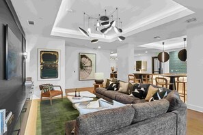 A modern living room with a sectional sofa, a coffee table, and a dining area with chairs and a table. - Walk to NoDa Arts District + Brew Pubs | King Bed (Charlotte)