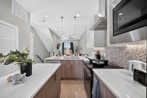 Een moderne keuken met een centraal eiland, houten kastjes en een grote televisie bevestigd boven het eiland.