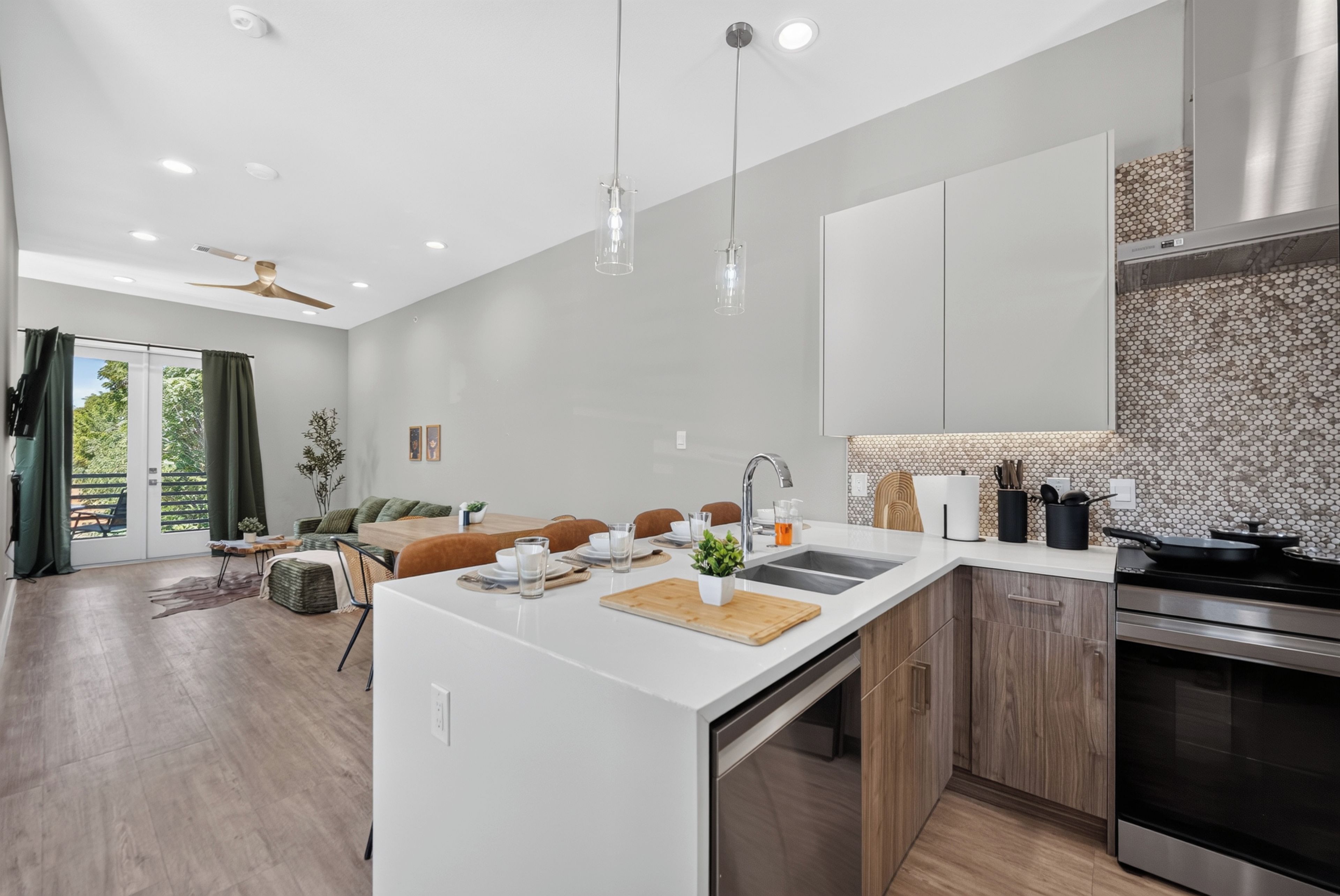 A modern kitchen with a central island, a dining area with a sofa and table, and a view through a glass door to an outdoor area.
