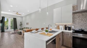 A modern kitchen with a central island, a dining area with a sofa and table, and a view through a glass door to an outdoor area.