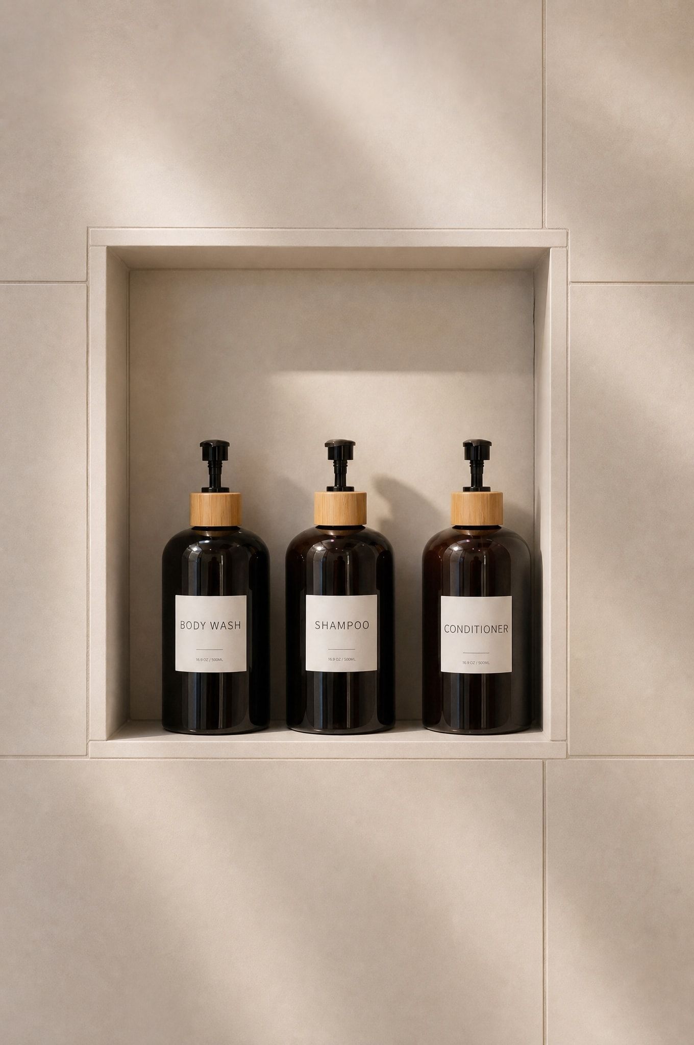 Trois bouteilles de gel douche, de shampoing et d’après-shampoing sont pos ées sur une étagère, contre un mur recouvert de carreaux.