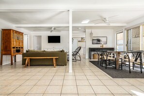 A spacious living area with a sofa, a wooden bench, a dining table with chairs, and a television mounted on the wall. - The Palms - private yard & parking, 200m to beach (Margate)
