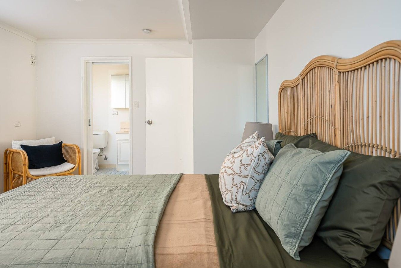 A bedroom with a bed, a chair, a door, and a wall with a textured pattern.