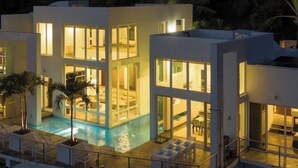 A modern two-story building with a swimming pool, large windows, and outdoor seating. - NEW! Dreamy & Spacious 5-bedroom house with generator in Cruz Bay with Pool (Cruz Bay)