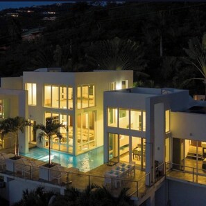 Un edificio moderno de dos pisos con piscina, ventanas amplias y mobiliario exterior.
