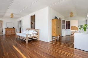 A spacious room with a wooden floor, a white sofa, a wooden cabinet, and a bed with a headboard.