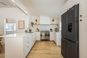 A modern kitchen with white cabinetry, a stainless steel oven, a black refrigerator, and a wooden floor.