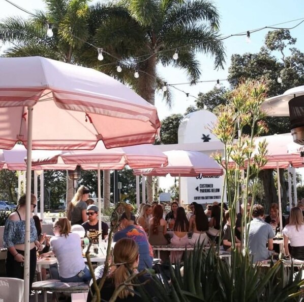 An outdoor seating area with tables and umbrellas, surrounded by palm trees and greenery.
