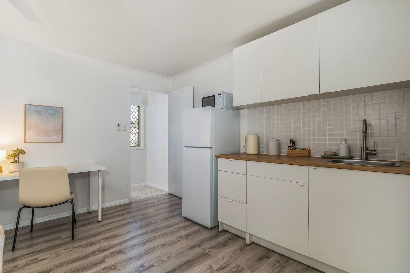 Eine kleine Küche mit weißen Schränken, einem Kühlschrank, einer Spüle und einer Holz Arbeitsplatte.