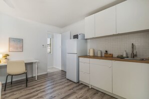 A compact kitchen with white cabinets, a refrigerator, a sink, and a wooden countertop.