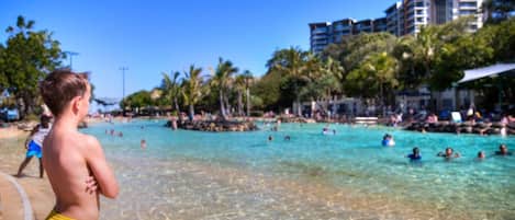 Une plage avec une eau cristalline, des palmiers et un bâtiment en arrière-plan.
