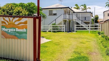 Imóvel residencial com área externa coberta, cerca branca e escadaria que leva a uma varanda.