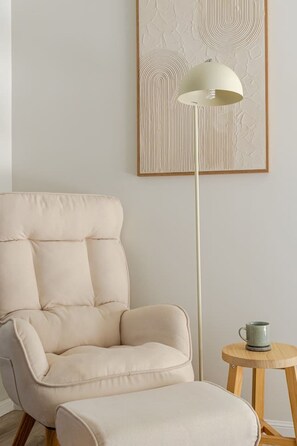 A room with a cream-colored armchair, a floor lamp, and a small wooden table with a cup.