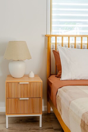 A bedroom with a wooden nightstand, a white lamp, and a bed with a brown headboard.