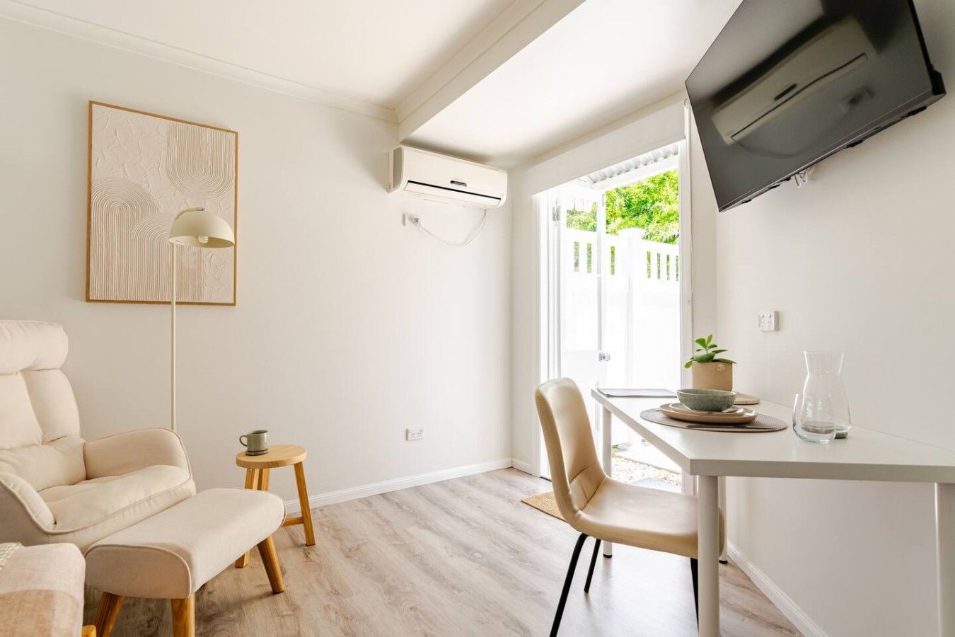Un salon moderne comprenant un canapé, une table à manger avec des chaises, une petite table d’appoint, un lampadaire et un téléviseur à écran plat fixé au mur.