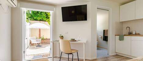 A modern, well-lit room with a dining area, a TV mounted on the wall, and a kitchen with a tiled backsplash.