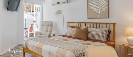 Un dormitorio con cama, una silla, televisor y aire acondicionado de pared.