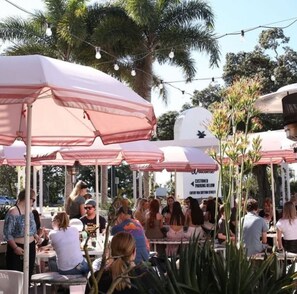 An outdoor seating area with tables and umbrellas, surrounded by palm trees and greenery. - Margate Beach studio 2 (Margate)