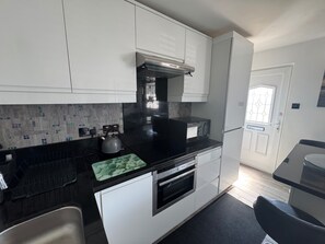 A modern kitchen with white cabinets, a black countertop, a kettle, a microwave, and an oven.