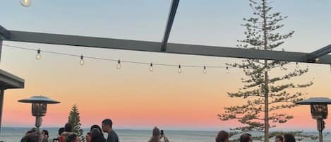 Ein Essbereich im Freien mit Tischen und Stühlen mit Blick auf ein Gewässer bei Sonnenuntergang.