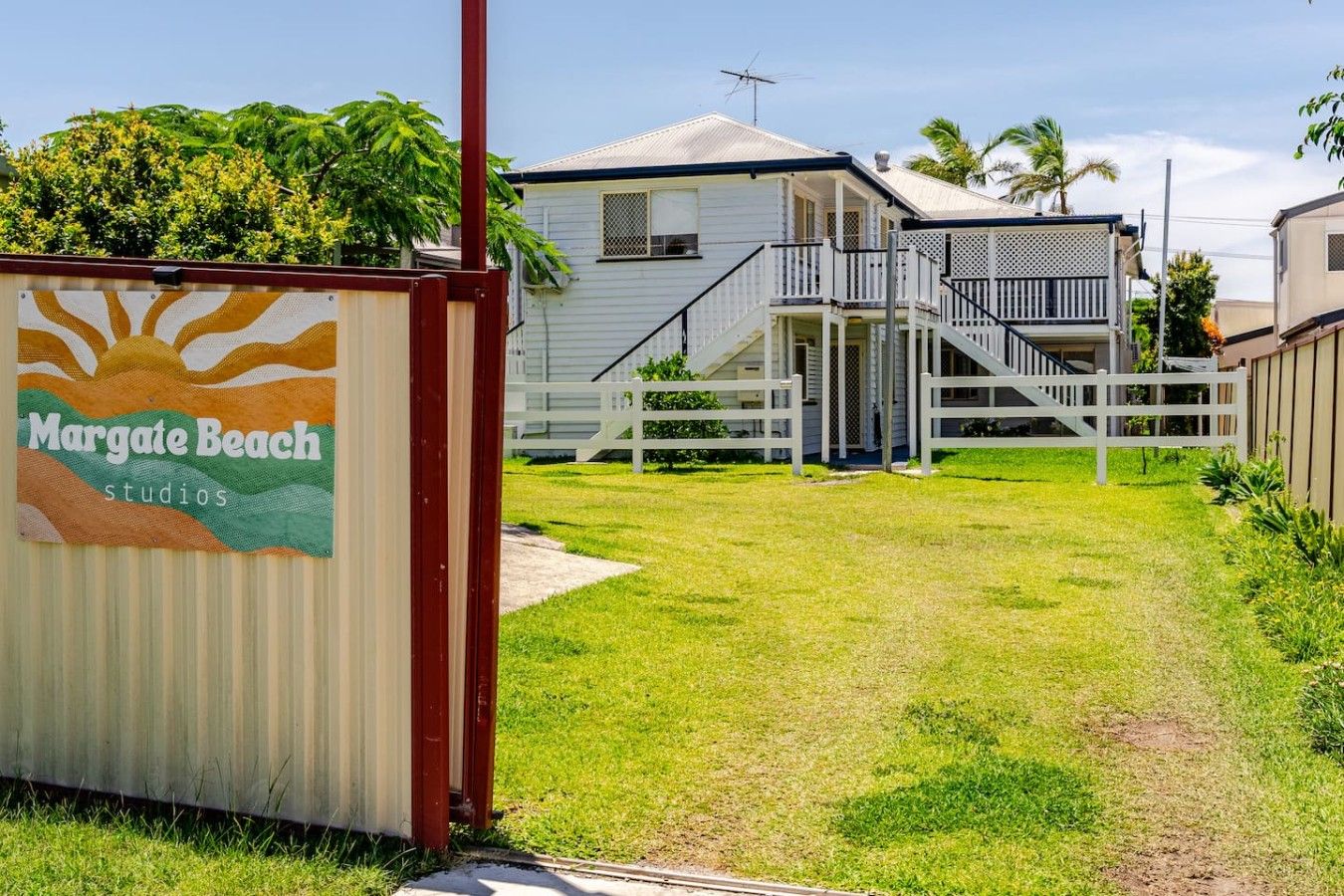 A residential property with a covered outdoor area, a white fence, and a staircase leading to a balcony.