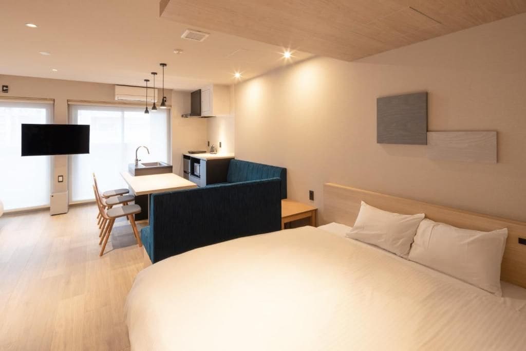 A hotel room with a bed, a desk, a chair, a TV, and a kitchenette.