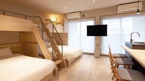 Habitació d'hotel amb llits superposats, escriptori amb cadires, televisió i finestra.