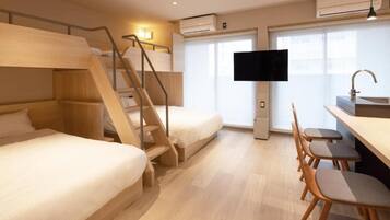 A hotel room with bunk beds, a desk with chairs, a television, and a window.