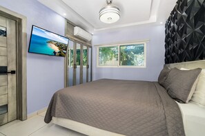 Ein Schlafzimmer mit einem Bett, einem an der Wand befestigten Fernseher und einem Fenster mit Blick auf Grünflächen.