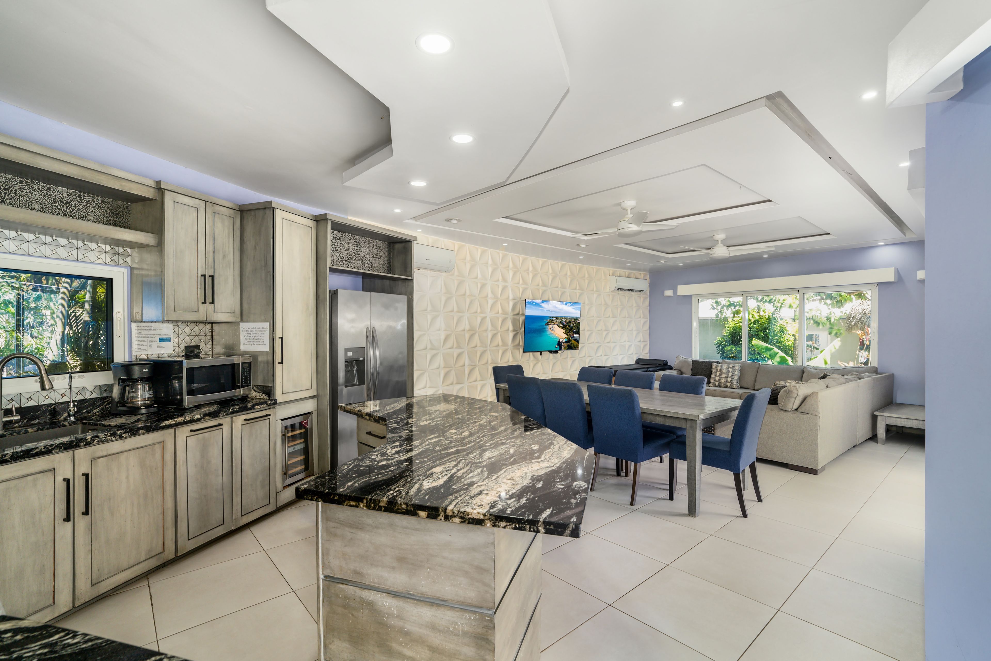 Una cocina moderna con comedor, con encimera de mármol, electrodomésticos de acero inoxidable y un televisor de pantalla plana montado en la pared.