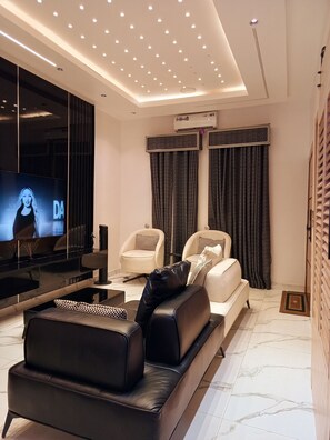 A modern living room with a flat-screen TV, leather sofa, armchairs, and a marble floor. - Your Home Away From Home – Comfort, Peace & Warm Hospitality (Lagos)