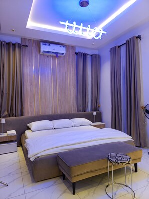 A modern bedroom with a large bed, an air conditioning unit, and a unique ceiling light fixture. - Your Home Away From Home – Comfort, Peace & Warm Hospitality (Lagos)