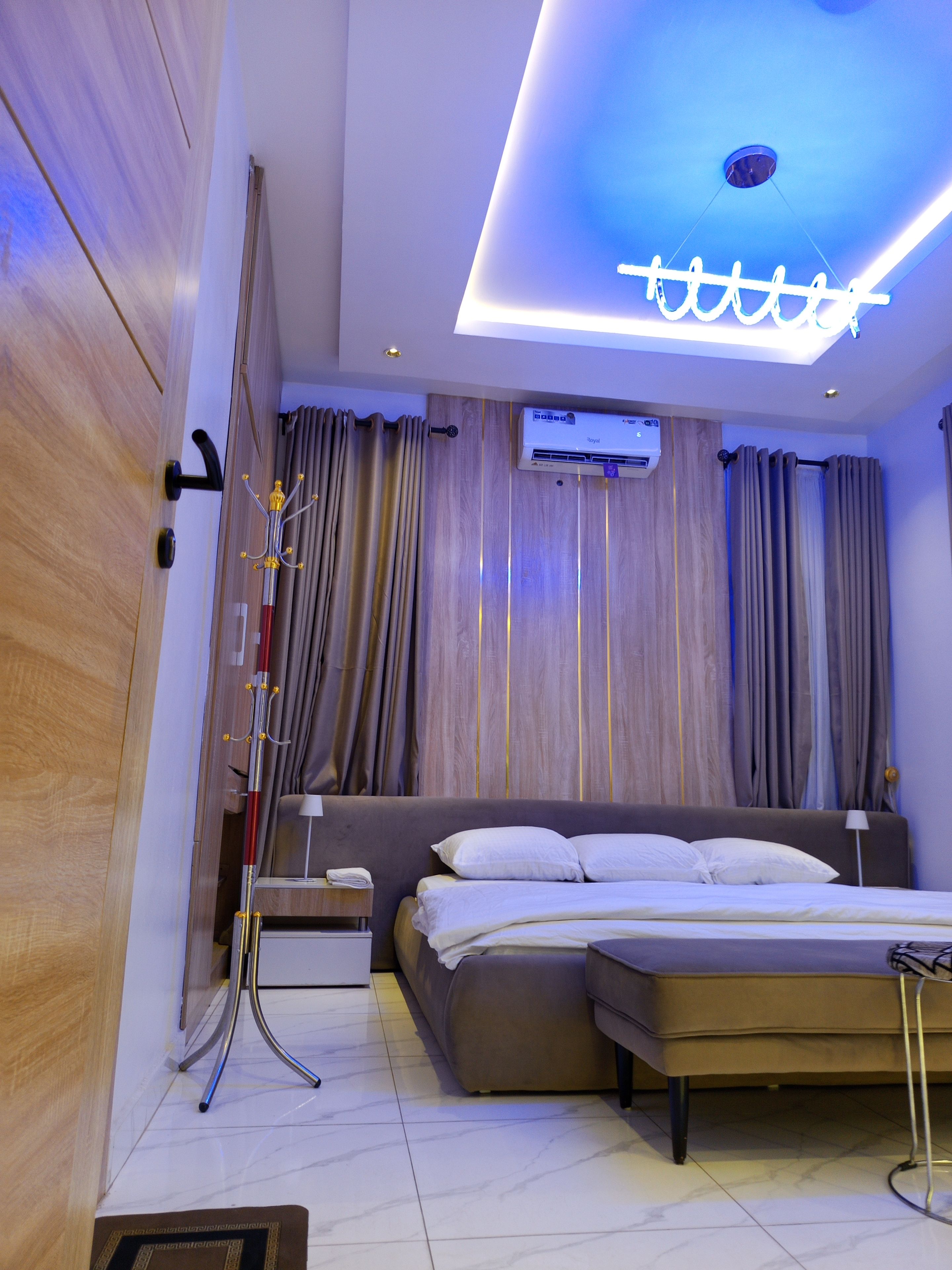 Quarto moderno com cama, mesas de cabeceira, luminária no teto e ar condicionado fixado na parede.