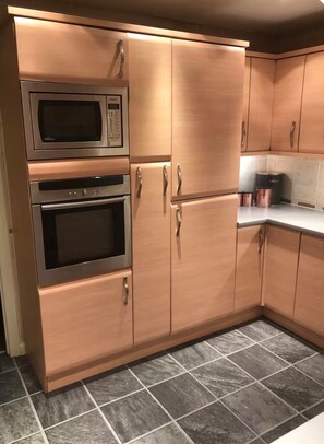 A kitchen with wooden cabinets, a microwave, an oven, and a coffee maker. - Apartment Sleeps 3 with WiFi (Alexandria)