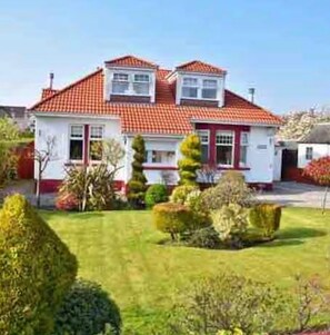 Una casa de dues plantes amb teulada de rajola vermella, un jardí ben cuidat i setges perfectament podades.