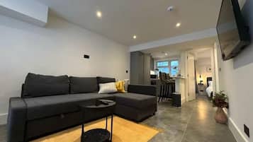 A modern living room with a sofa, a coffee table, and a flat-screen TV mounted on the wall.