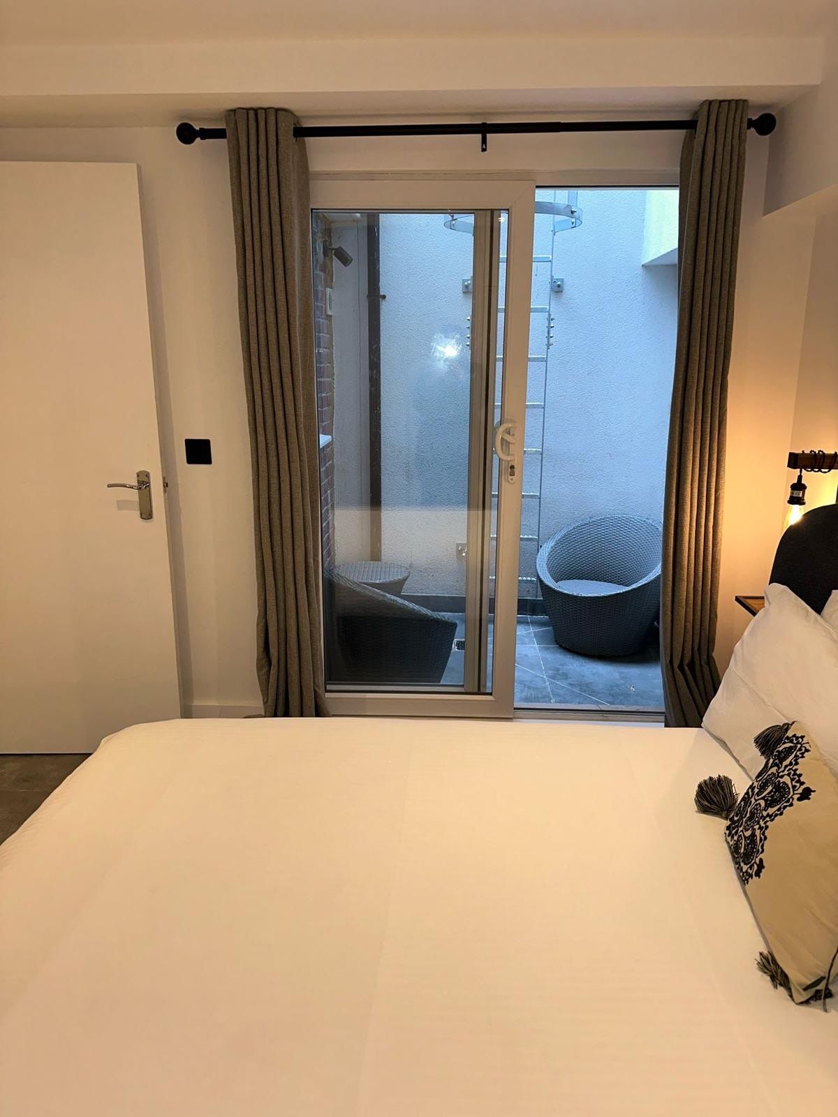 Une chambre d’hôtel avec un lit, une porte-fenêtre coulissante donnant sur un espace extérieur aménagé, et une vue sur l’extérieur.