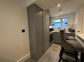 A compact kitchen with a built-in oven, a dining area with a single chair, and a window with a view. - Two Bedroom House In Kilburn (London)