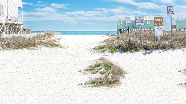 Uma trilha de areia leva a um edifício com várias janelas e uma varanda.