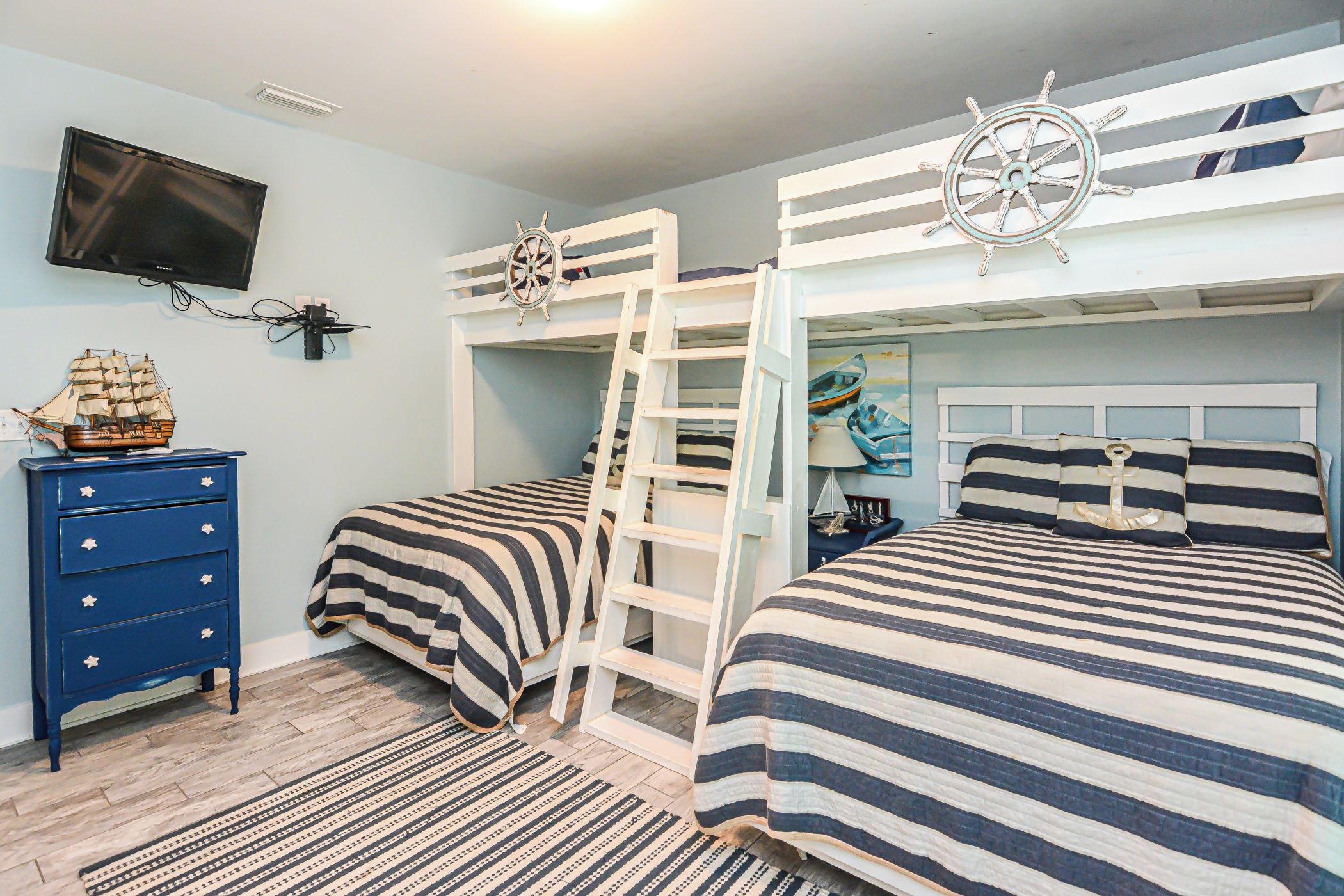 A bedroom with bunk beds, a dresser, a TV, and nautical-themed decor.