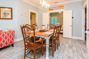 Une salle à manger avec une table et des chaises en bois, un lustre et un canapé rouge à motifs.