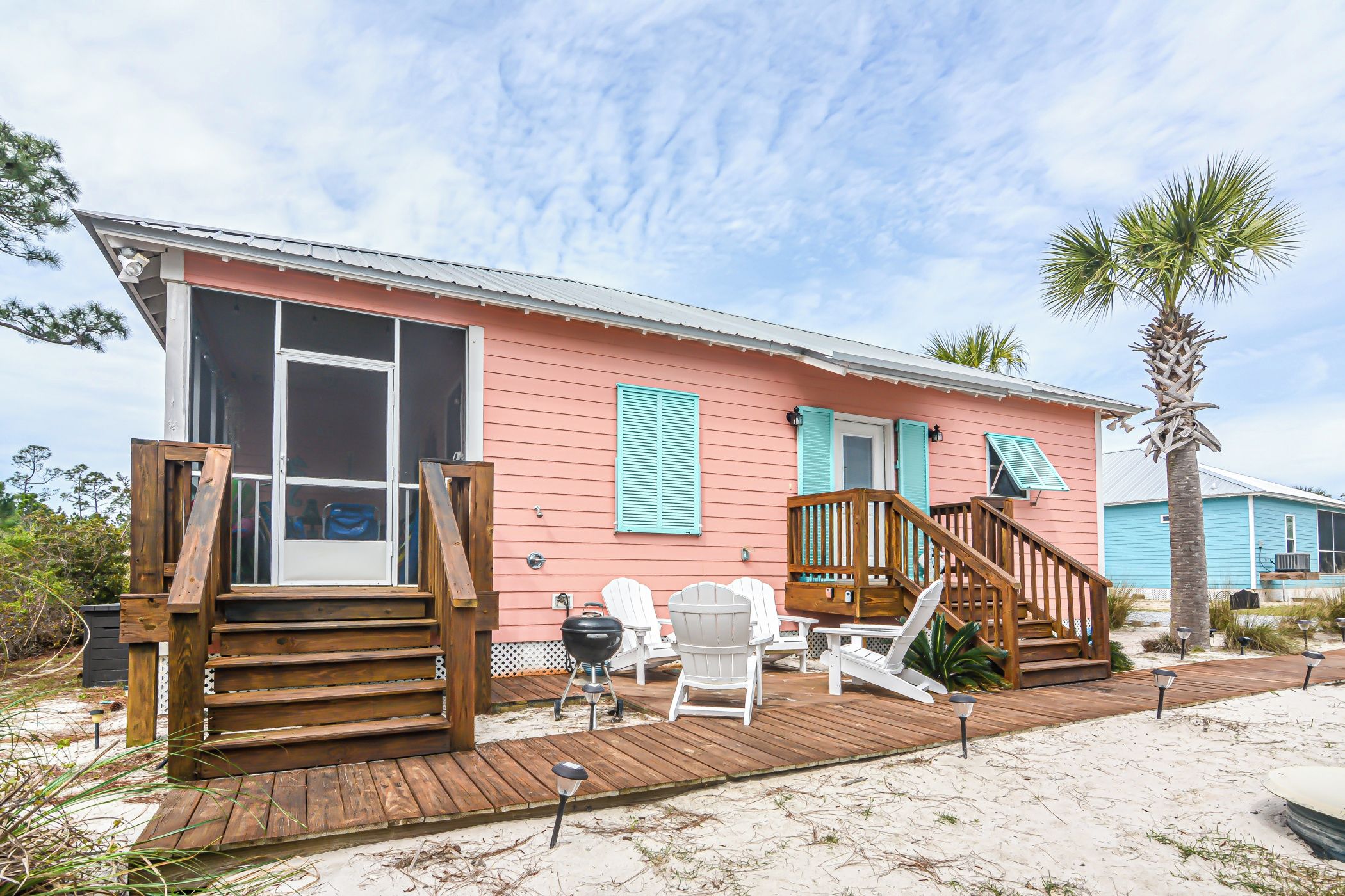 A beachfront property with a wooden deck, outdoor seating, and a staircase leading to the entrance.