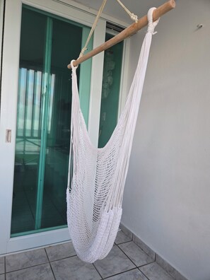 A white hammock hanging from a wooden beam, with a glass door and a tiled floor in the background. - Unforgettable, stunning Oceanfront modern condo! (Luquillo)