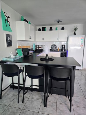 A modern kitchen with white cabinets, a black countertop, and a dining area with black chairs. - Unforgettable, stunning Oceanfront modern condo! (Luquillo)