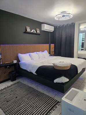 Une chambre à coucher moderne, équipée d’un lit, de tables de chevet, d’un climatiseur fixé au mur et d’un luminaire suspendu au plafond.