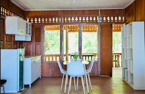 Un interior de madera con zona de comedor, cocina y vistas a través de un ventanal grande.