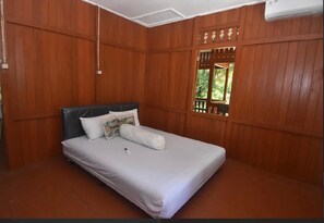 A single bed with a white mattress and pillows, a wooden headboard, and a window with a wooden lattice design.