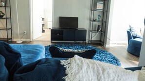 A living room with a sofa, a television, and a bookshelf. - 2-bedroom apartment in pleasant Huntsville with AC and fitness room (Huntsville)
