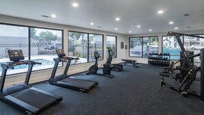 Een fitnessruimte met loopbanden, een crosstrainer en krachtapparaten, grote ramen met uitzicht op buiten.
